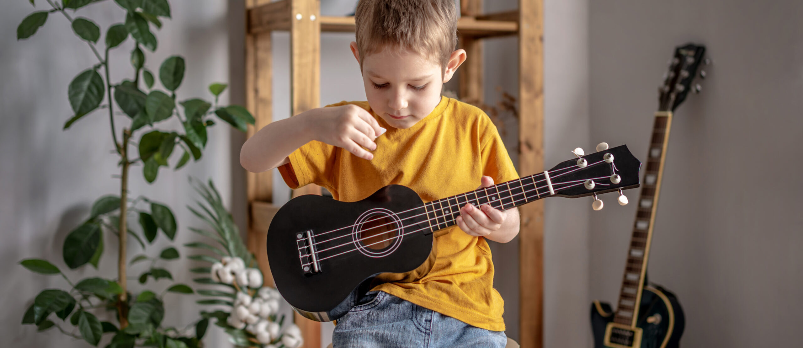 Cute cheerful boy is playing ukulele guitar in the music room. Joyful learning to play musical instruments.