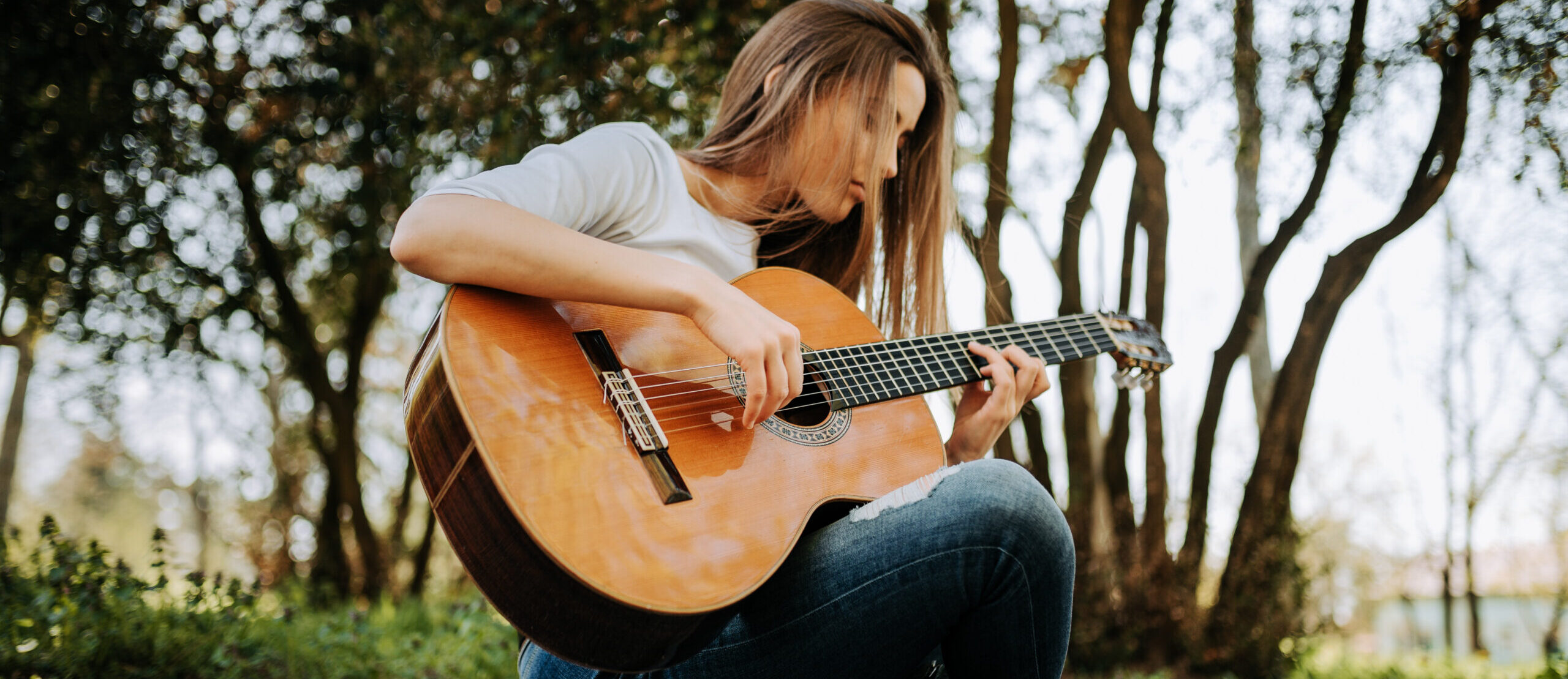 Young peaceful girl playing acoustic guitar in the park.